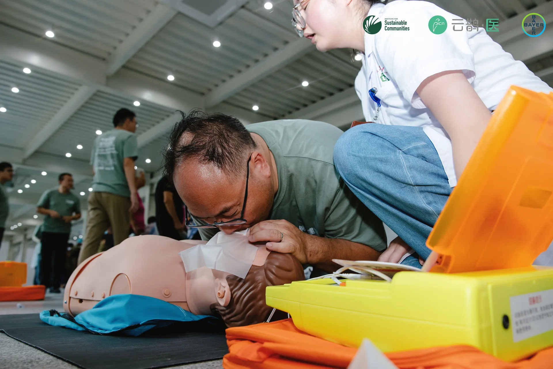 A participant practising CPR beside an AED training kit